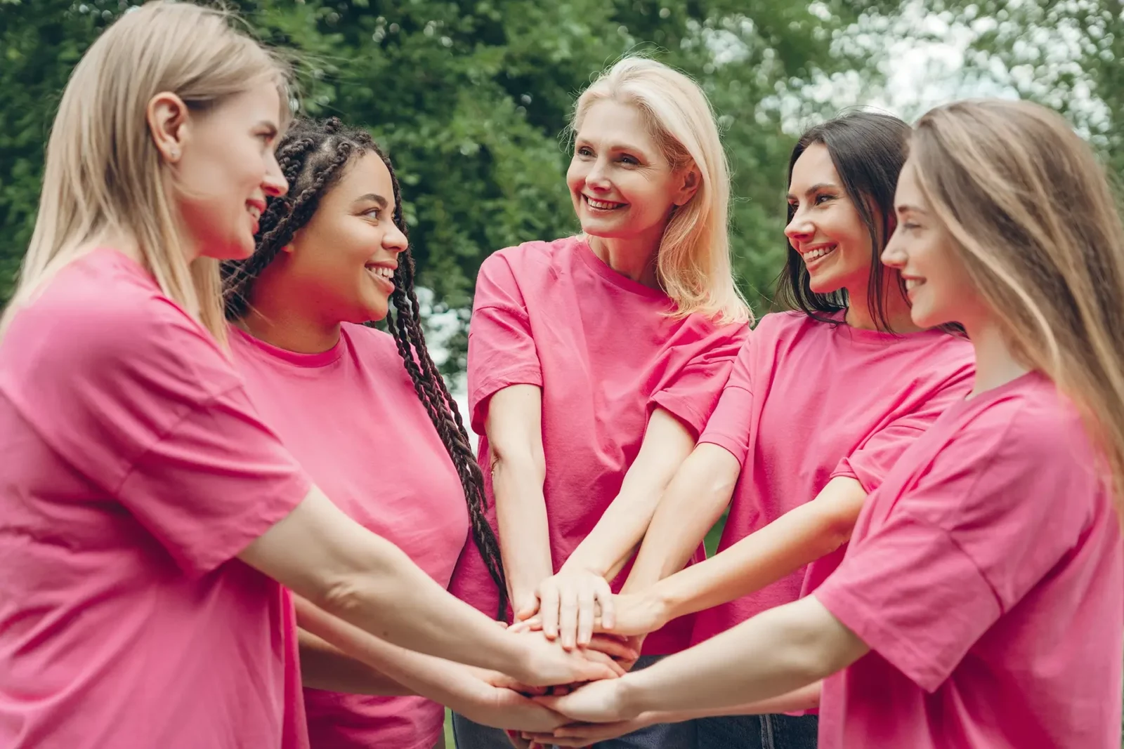 Fünf Frauen in rosafarbenen Hemden stehen im Freien in einem Kreis