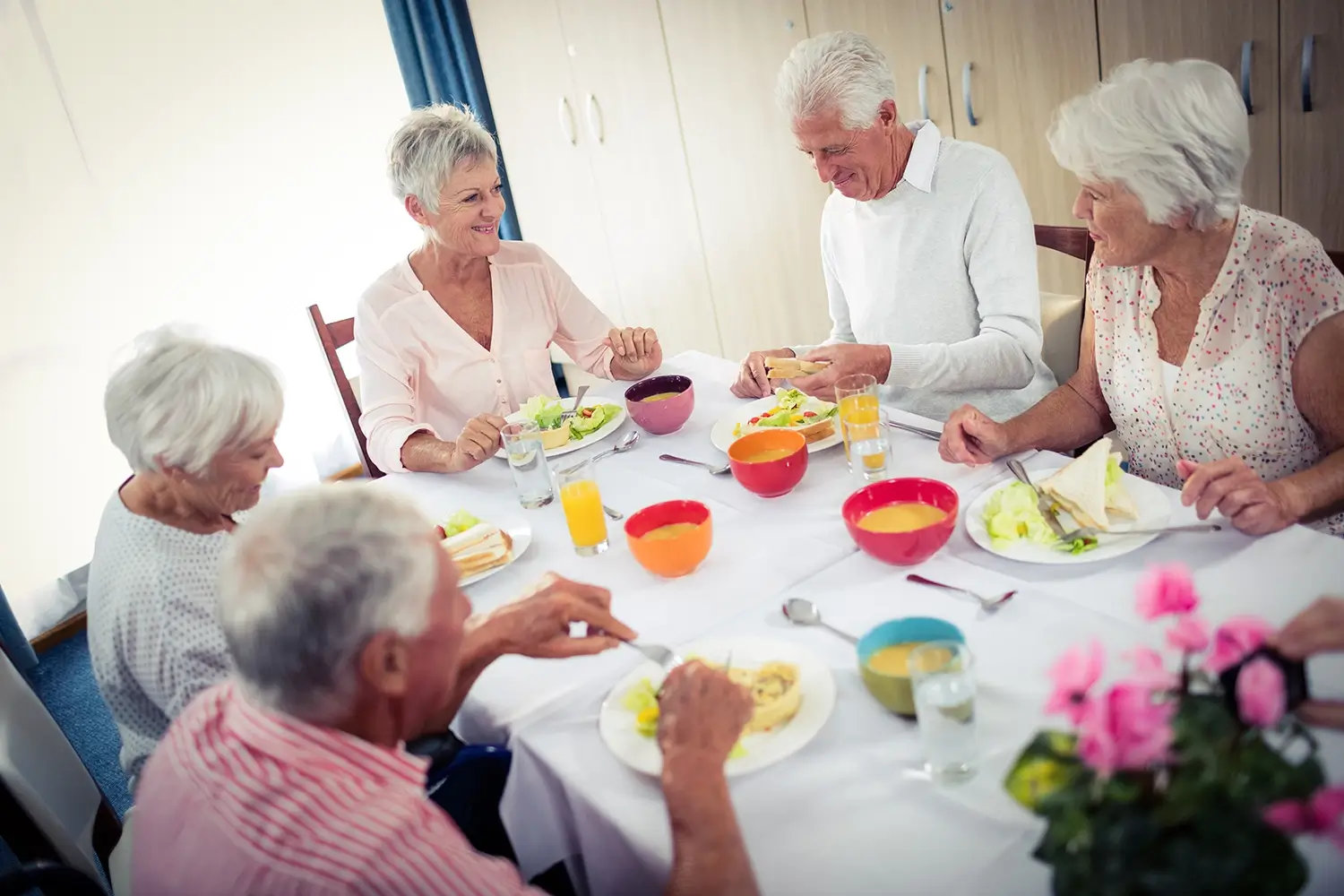 Fünf ältere Menschen sitzen um einen Tisch, essen gemeinsam und lächeln.